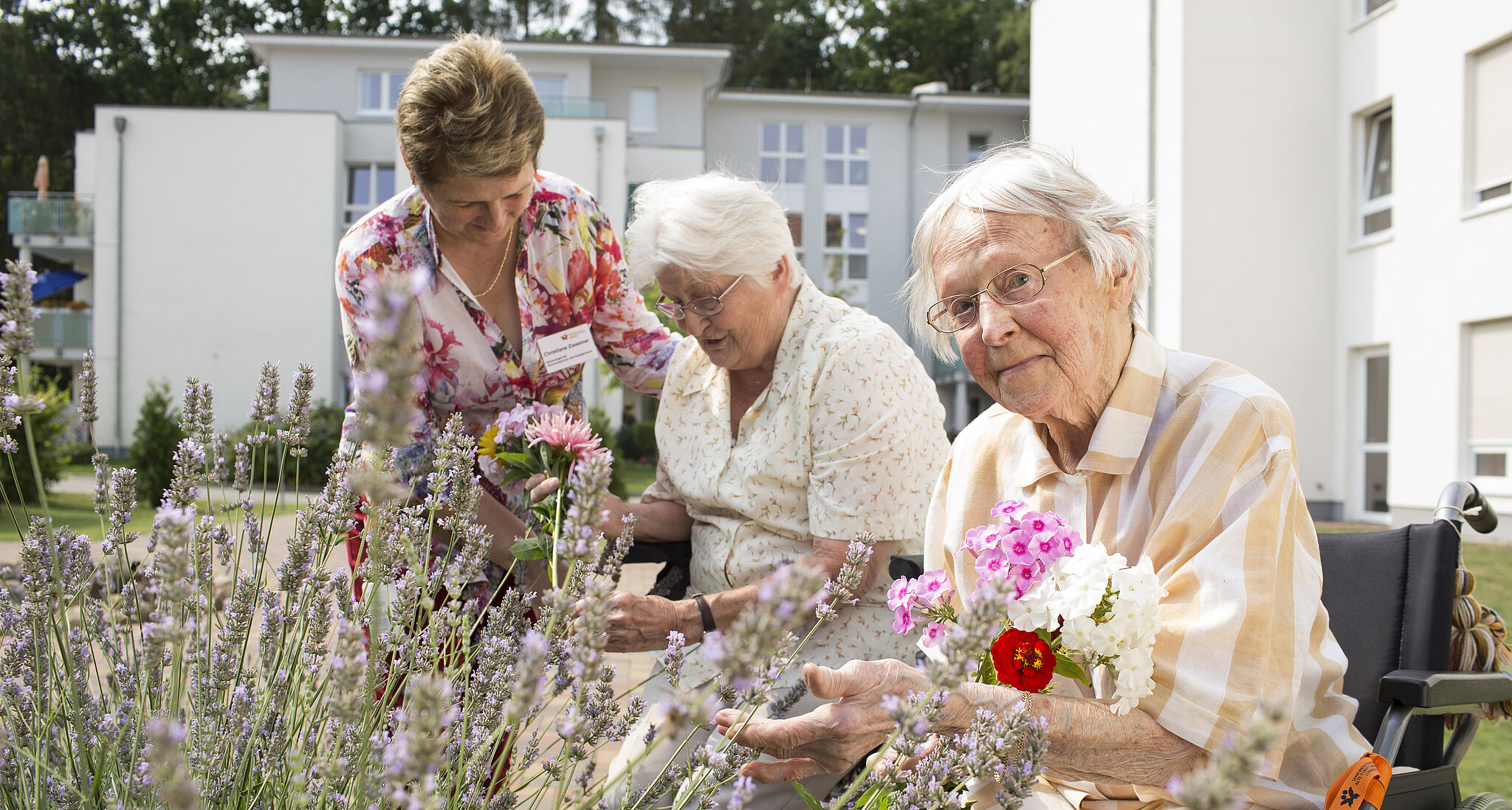 Zwei Bewohnerinnen pflücken mithile einer Betreuungskraft Blumen im Innenhof des Seniorenzentrums alte Stadtgärtnerei
