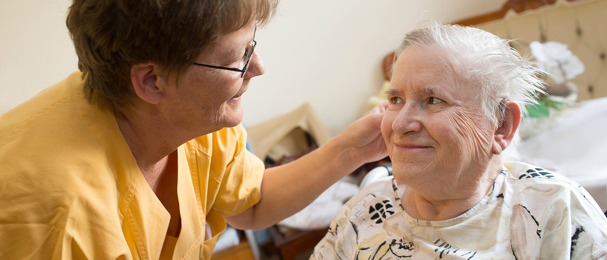 Eine Altenpflegerin hilft einer Bewohnerin beim Einsetzen ihrer Hörgeräte
