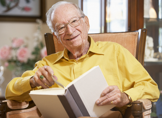 Ein ältere Mann sitzt in einem Sessel und blättert in einem Buch